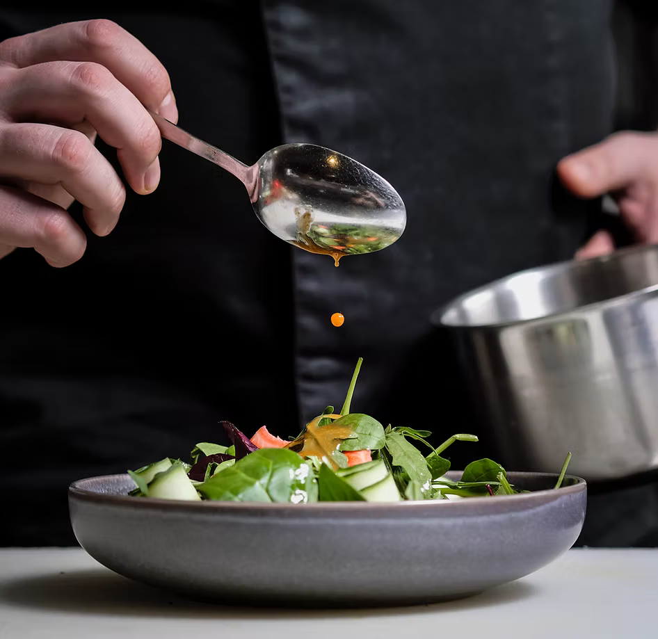 Chef adding dressing to a salad with a spoon