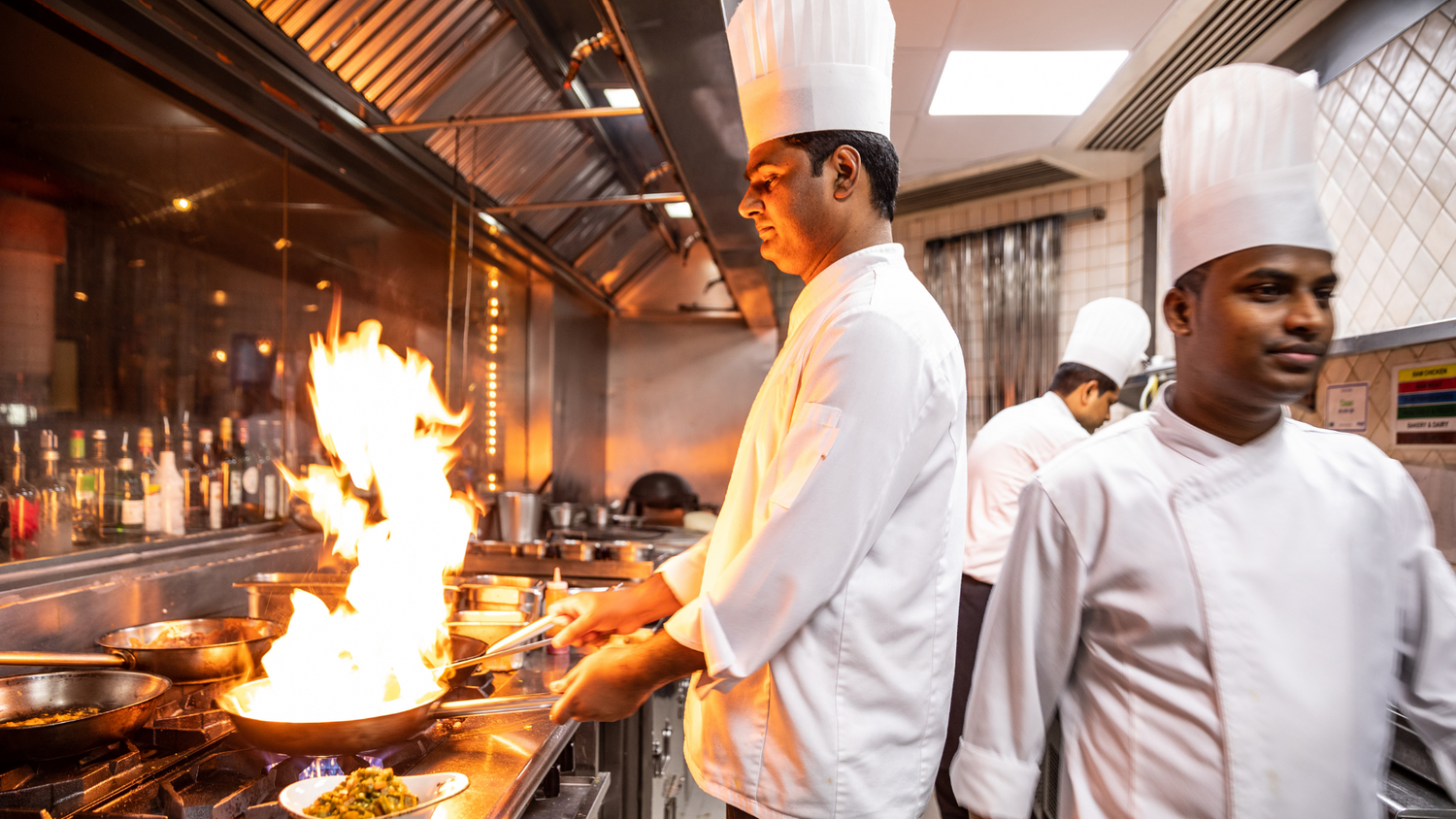 Chefs in a kitchen with flames and cooking equipment