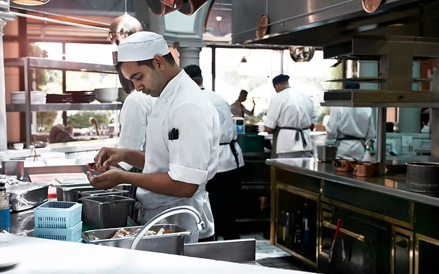 Chefs working in a busy kitchen with stainless steel equipment and various kitchenware.