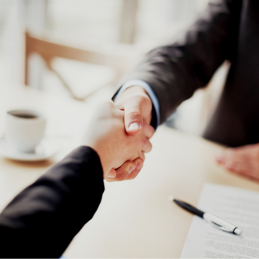Two people shaking hands at a desk with a cup and documents in the background