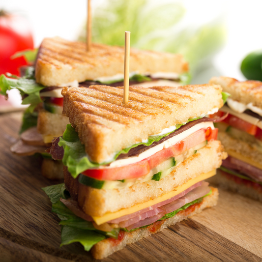 Club sandwich cut in half on a wooden board with fresh vegetables in the background