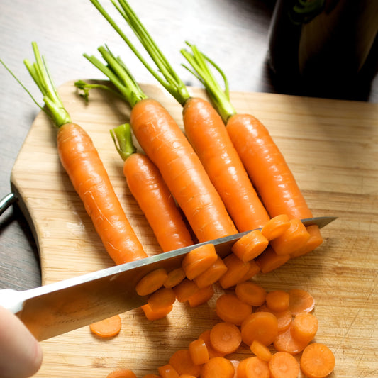 Carrots being chopped on a wooden cutting board with a knife.